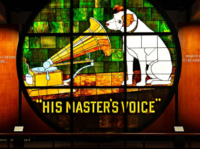 Glass image of dog listening to a phonograph with the words "his master's voice" at a display 